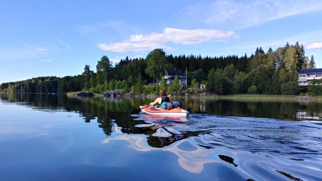 Kajakfahrer auf dem Dalsland Kanal. Im Hintergrund steht ein Ferienhaus in Dalsland.